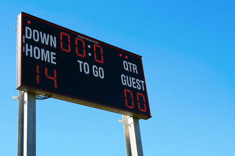 Learning Center 20 A football scoreboard displays Home: 14, Guest: 0 with 0:00 time remaining, under a clear blue sky.